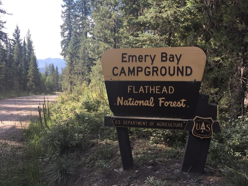 Gravel road winds into a forested area beside a two-tone campground sign in Glacier National Park.