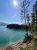 Emery Bay shoreline in Glacier National Park with turquoise water, pine trees, and a sunlit sky.