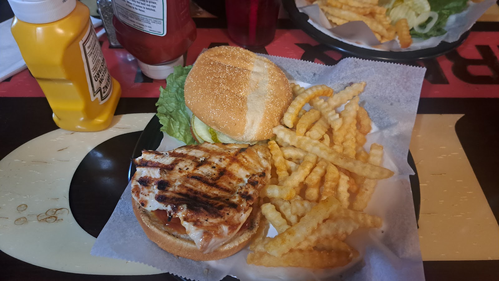 Grilled chicken sandwich with lettuce and crinkle-cut fries at Glacier National Park, eaten at a lodge-style restaurant setting.