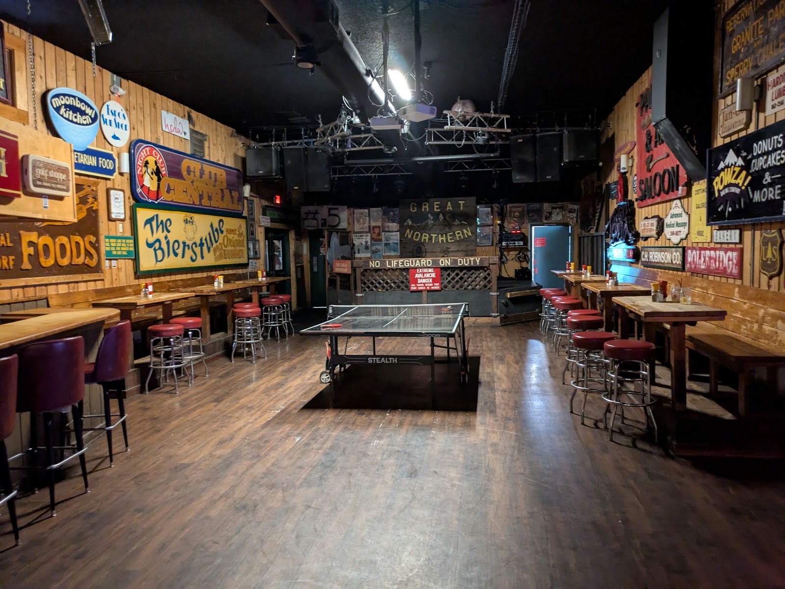 Interior of a rustic bar in Glacier National Park with wooden walls and vintage signs, centered by a table tennis setup.