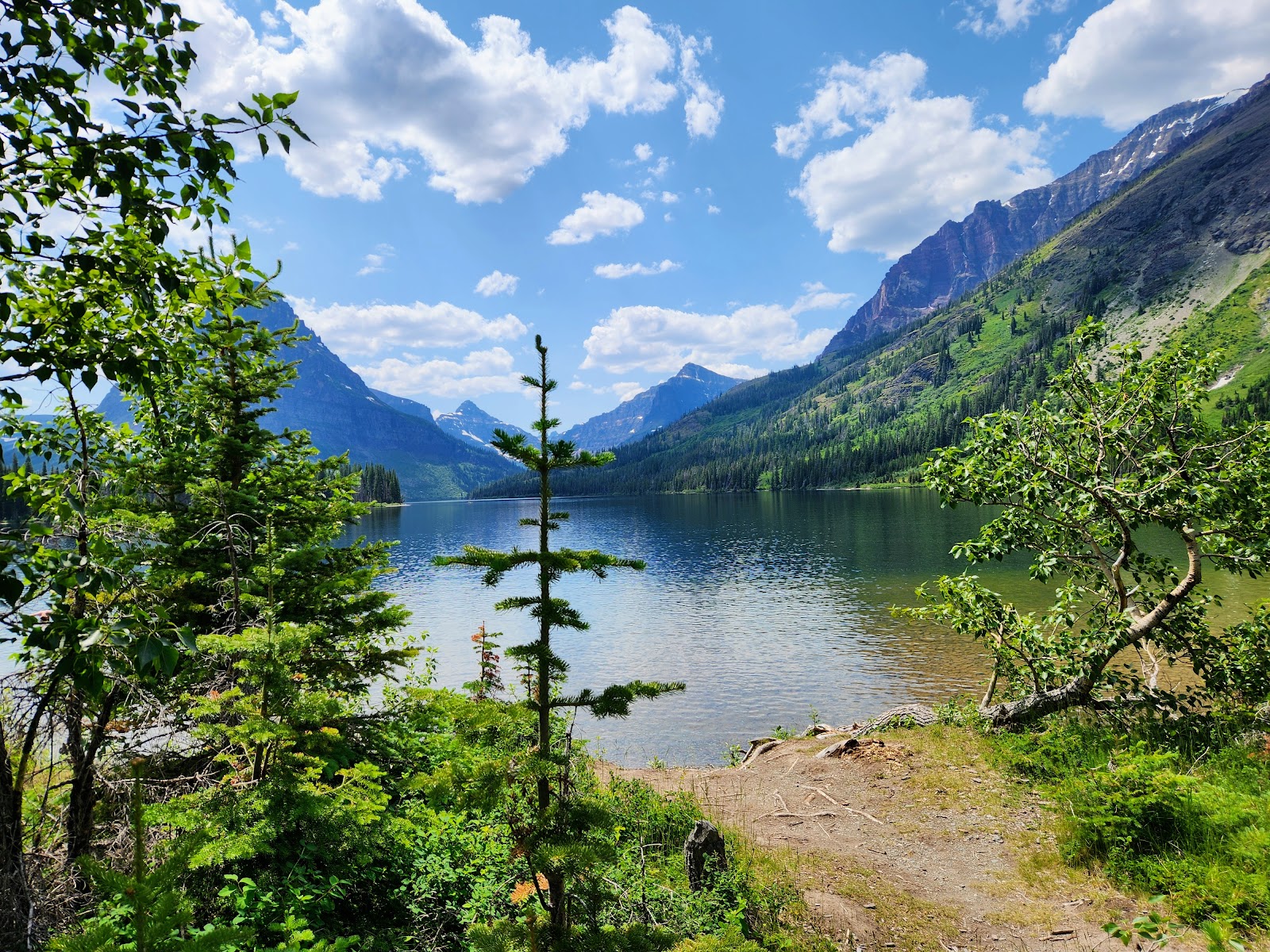 Two Medicine Picnic Area, Glacier National Park, with a calm lake framed by pine trees and rugged, snow-capped peaks in the distance.