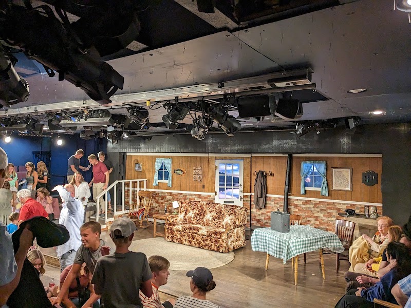 Cozy theatre interior with a living-room set, wood-paneled walls, and an audience gathered in Yellowstone National Park.