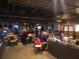 Cozy Glacier National Park restaurant interior filled with people at wooden tables and couches.