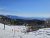 Snowy ski slope with a chairlift and pine forest below Glacier National Park, distant mountains under a clear blue sky.