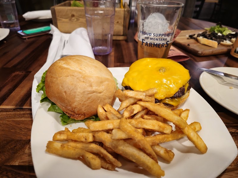 Cheeseburger with melted cheese and lettuce, golden fries, and a beer glass on a wooden table in Yellowstone National Park restaurant.