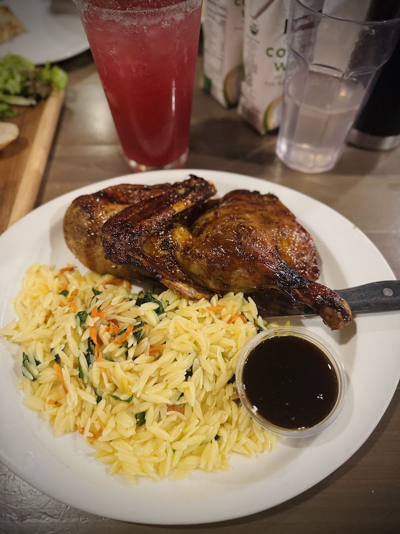 Roasted chicken leg with herb rice and mixed vegetables on a plate, a small dark sauce cup, and a tall red drink in Yellowstone National Park.