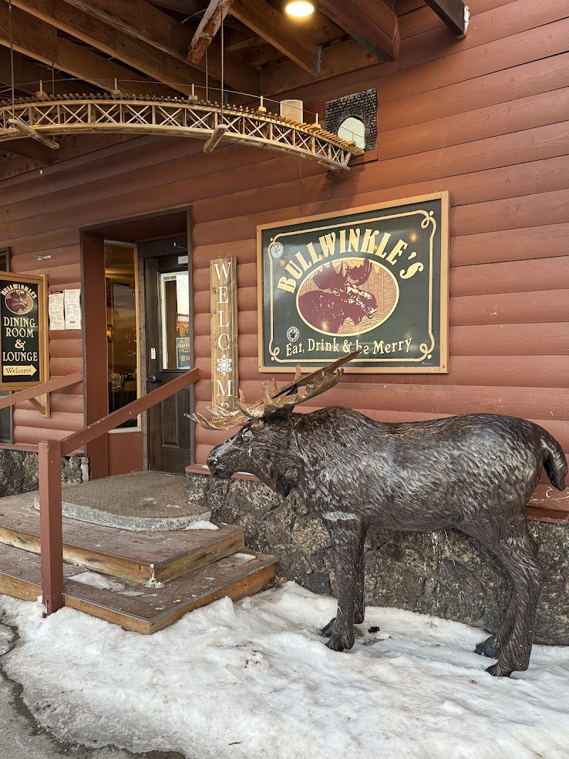 Rustic lodge entrance in Yellowstone National Park with a large moose statue, signs, and a model train above the doorway.