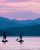 Paddleboarders glide on a calm lake at sunset with blue mountain silhouettes behind, in Glacier National Park.