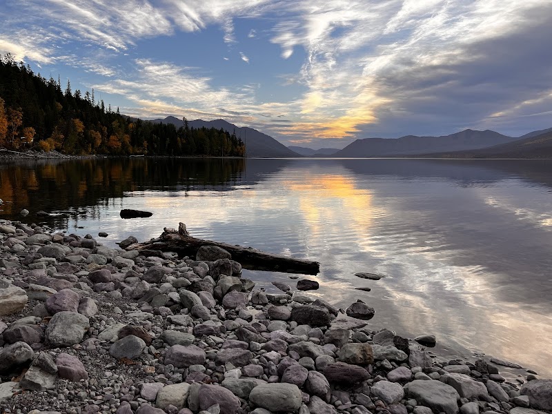 Sunset over Lake McDonald in Glacier National Park, calm water reflecting a fall forest and distant mountains.