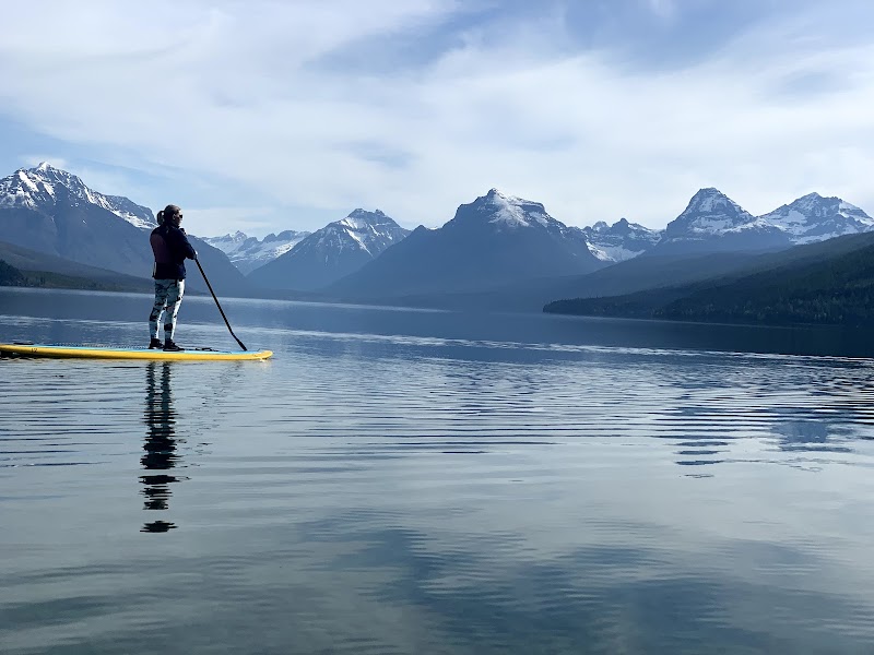 Paddleboarder on calm Lake McDonald at Glacier National Park with snowcapped peaks and reflections.
