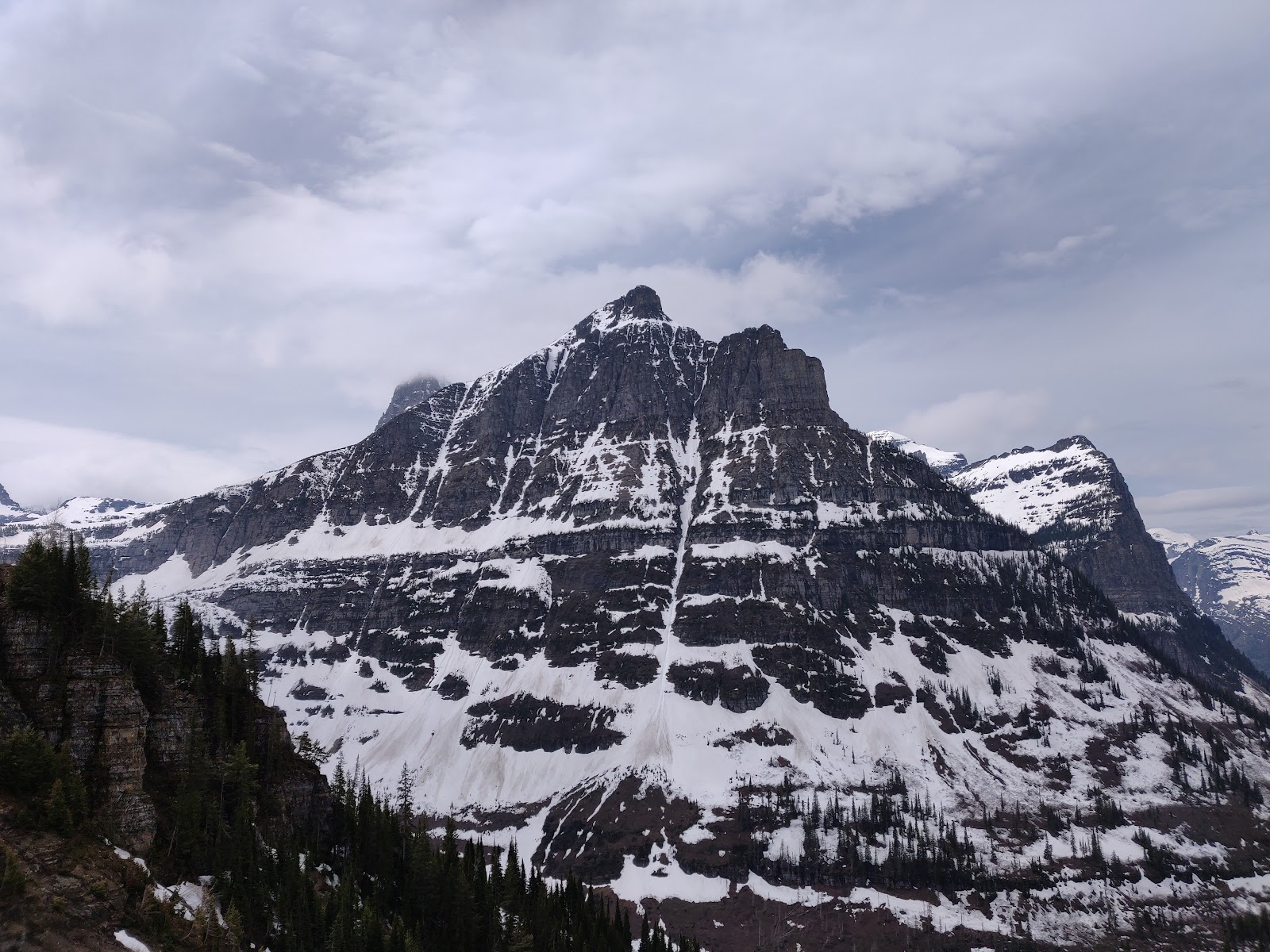 Snow-dusted jagged peaks rise over pine forests and snowy slopes in Glacier National Park