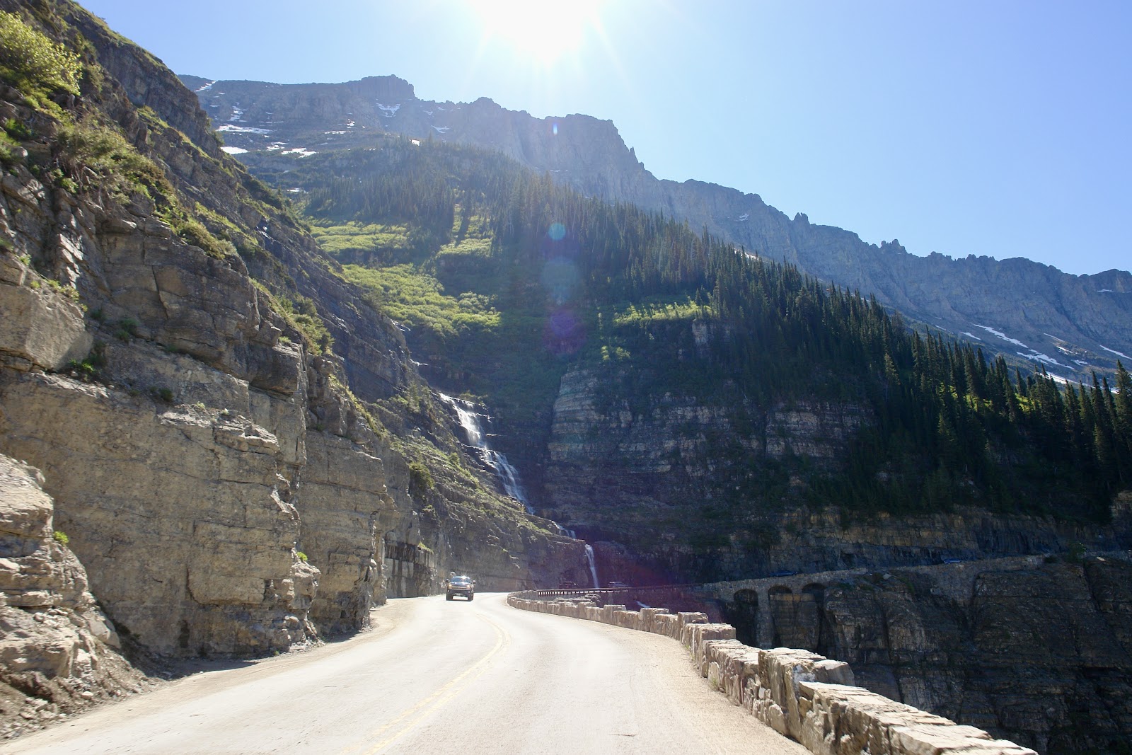 Winding mountain road along a canyon with a waterfall and dense pine forest in the Glacier National Park wilderness corridor