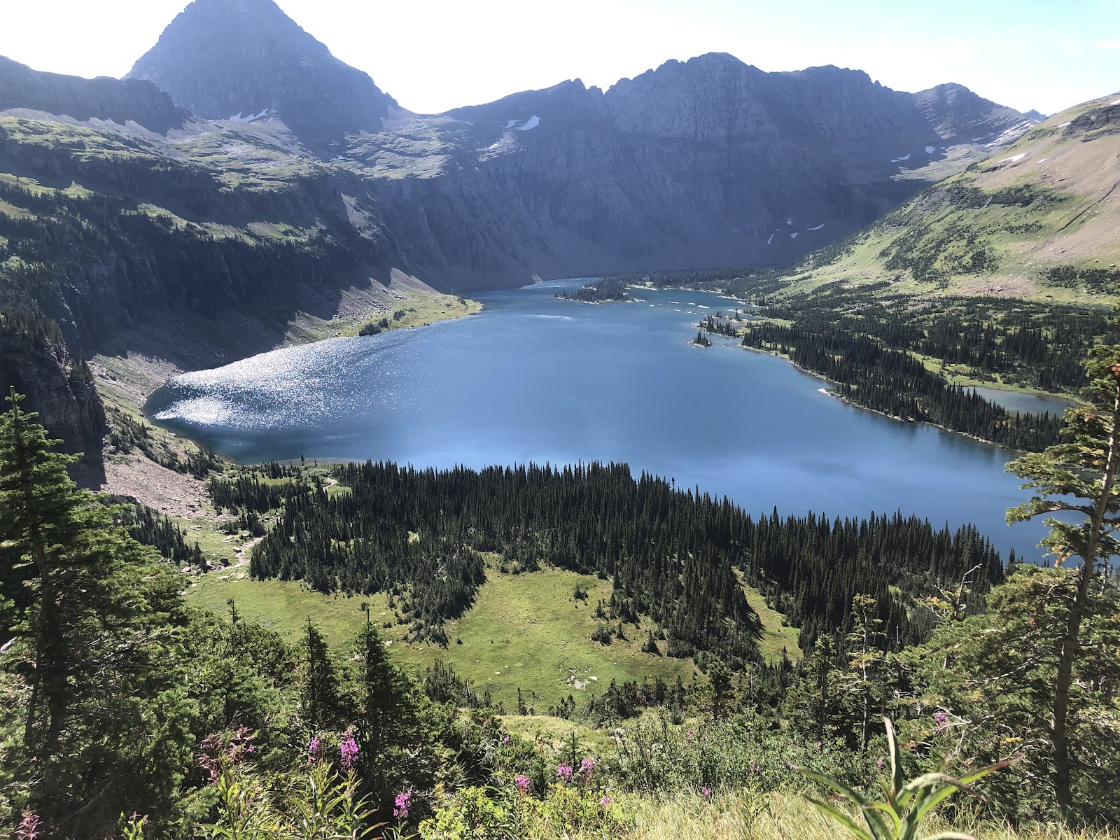 Glacier National Park: a bright blue alpine lake in a valley, encircled by rugged peaks, slopes, and dense evergreens.