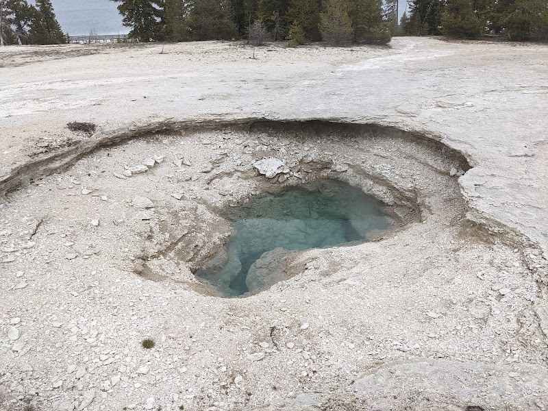 Geothermal pool with turquoise water surrounded by white mineral ground at a Yellowstone National Park overlook.