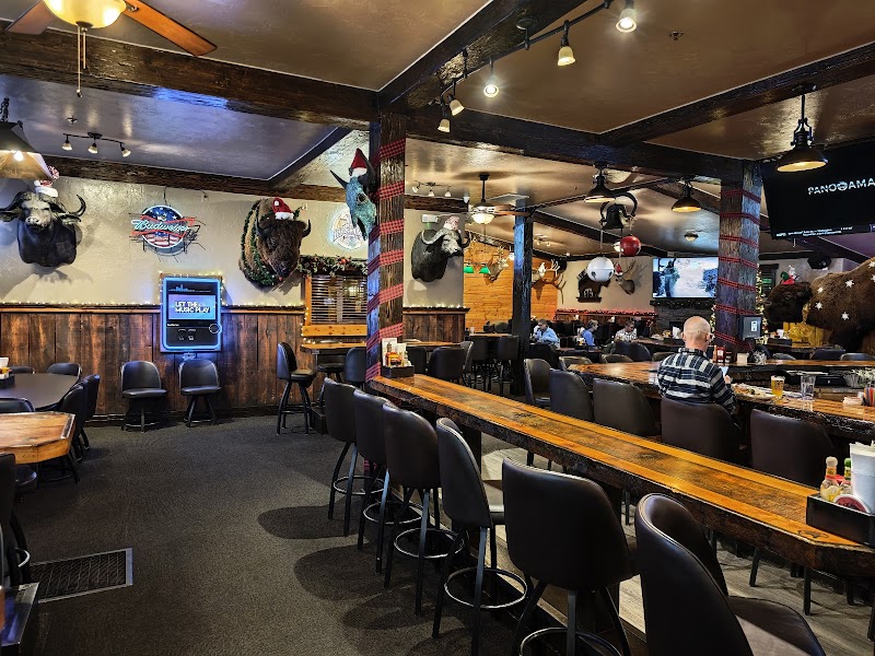 Cozy restaurant interior with wooden beams, long bar, black stools, mounted animal heads, and diners in Yellowstone National Park.