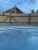 Wooden fence with a concrete-edged pool in the foreground; a log-cabin roof peeks over the fence under a blue sky in Yellowstone National Park.