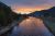 Sunset over a winding river at a Yellowstone National Park campground, with pines, grassy banks, and distant mountains.