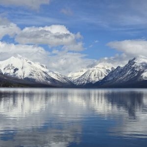 Apgar Beach on Lake McDonald with snow-capped peaks and a tranquil reflective lake in Glacier National Park.
