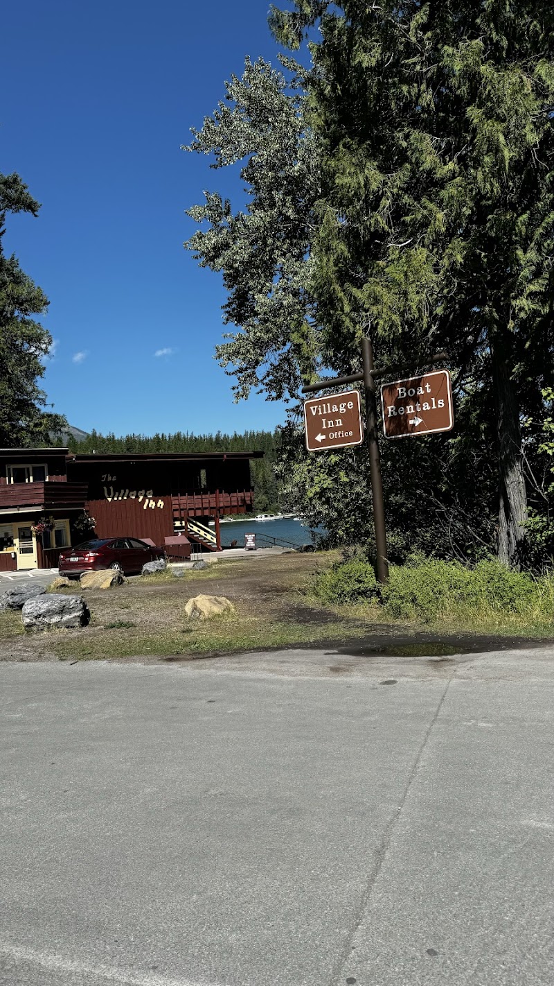 Apgar Beach on Lake McDonald in Glacier National Park with a lakeside lodge and pine trees nearby, under a clear blue sky.