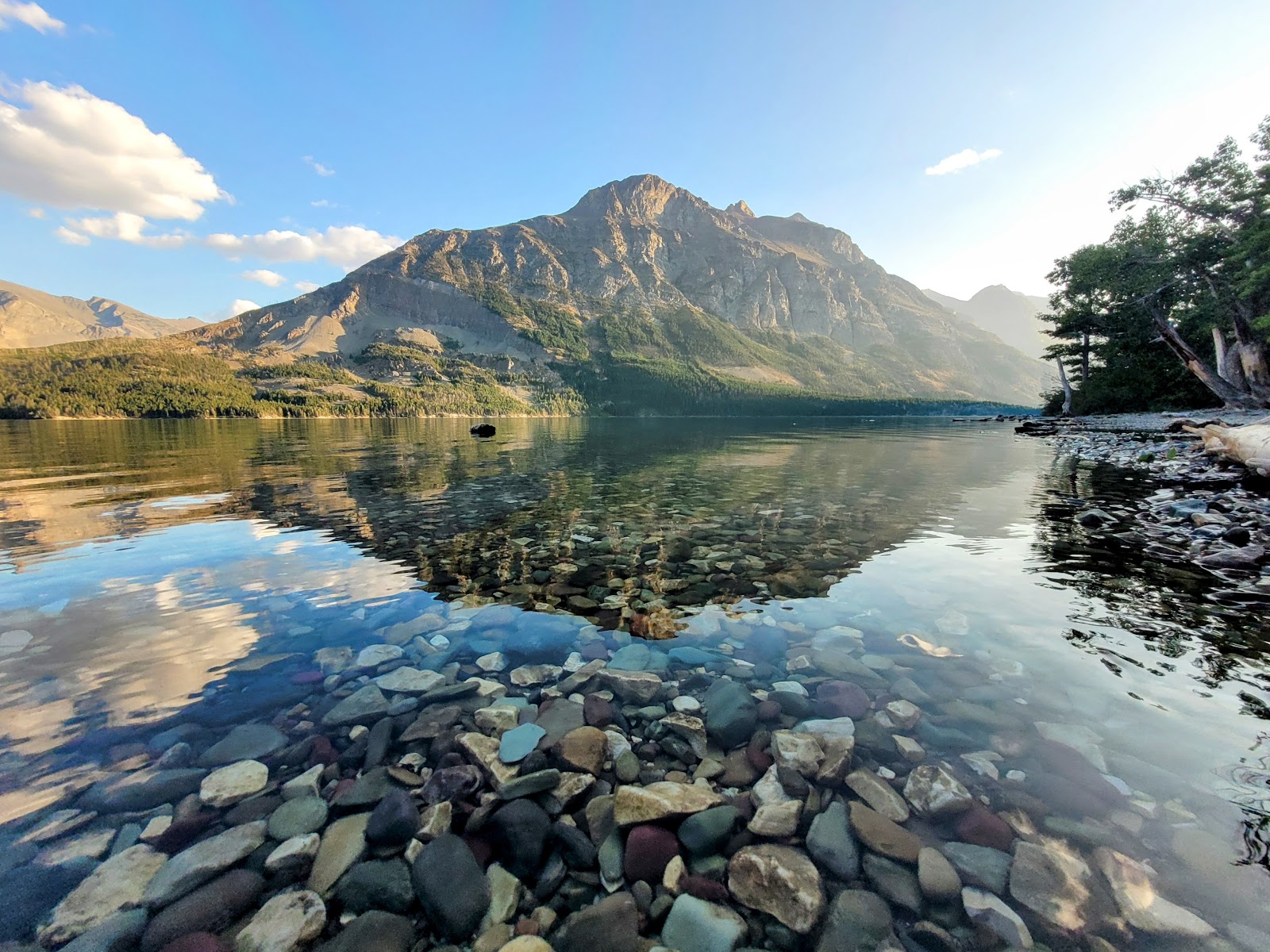 Rising Sun Picnic Area at Glacier National Park with a rocky lakeshore and towering mountain reflected in calm water.