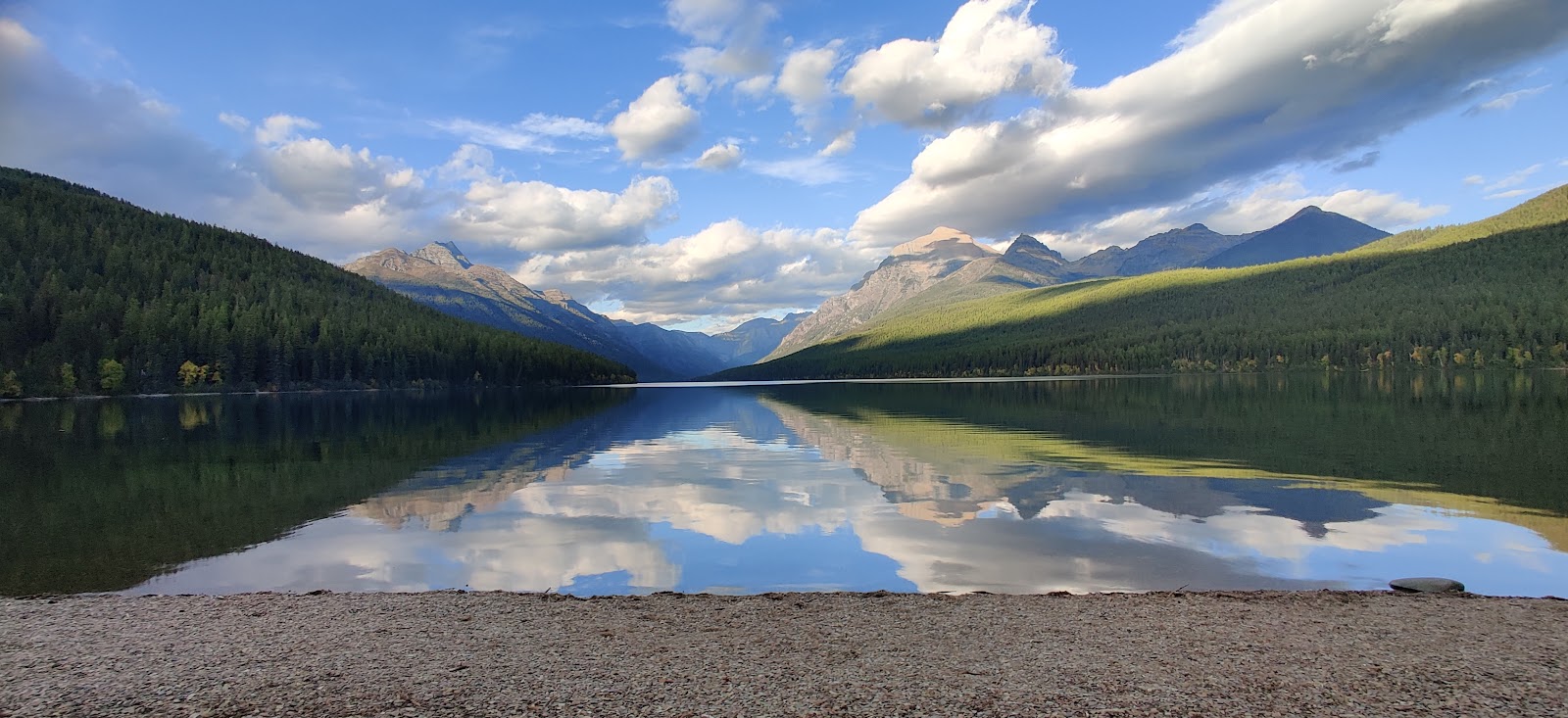Rainbow Peak lake view in Glacier National Park reflecting the surrounding green forests and blue sky.
