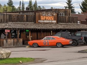Rustic Montana tap house in Glacier National Park with a bright orange 01 race car parked out front.