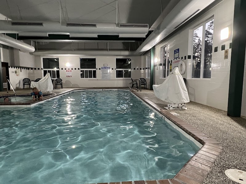 Indoor hotel pool in Yellowstone National Park lodge with turquoise water, white tile walls, and draped lounge chairs along the deck.