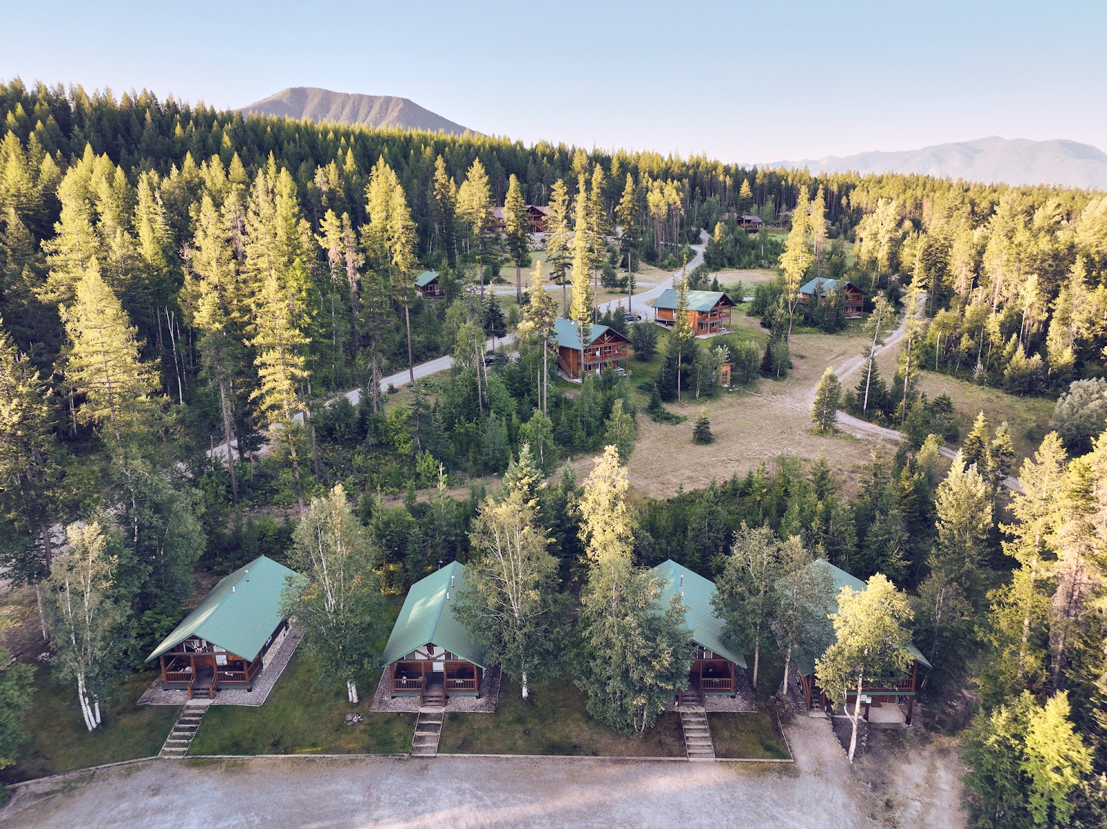 Paddle Ridge cabins sit among evergreen pines at Glacier National Park, offering forested lodge-style lodging with green roofs.
