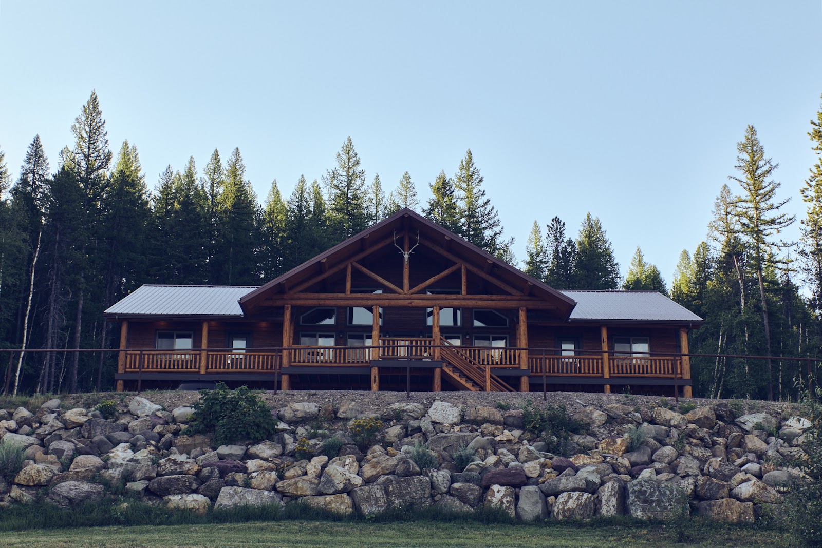 Rustic log lodge gift shop building at Glacier National Park with a stone terrace and evergreen forest backdrop.