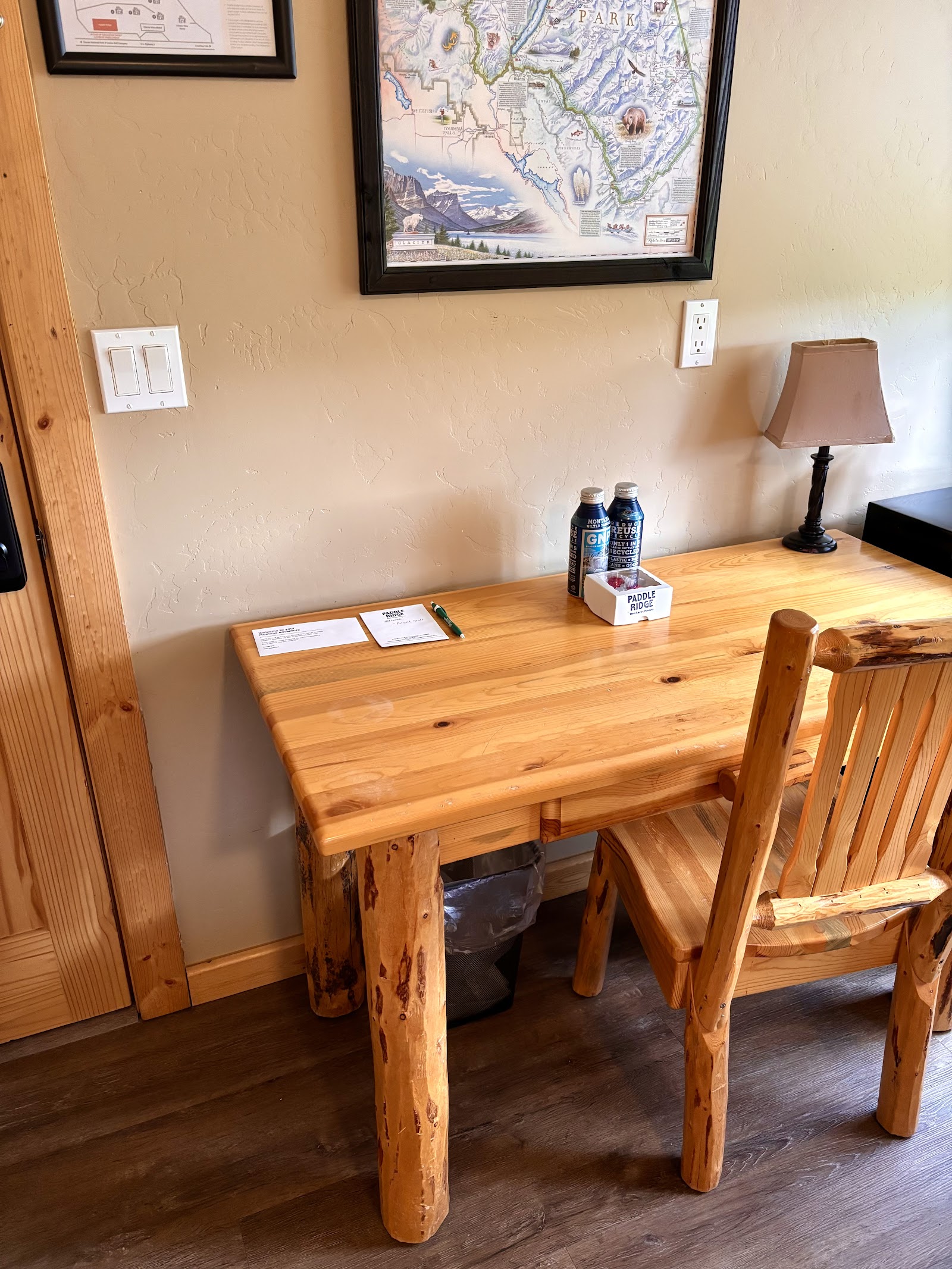 Rustic wooden gift shop counter inside Glacier National Park, with framed maps on the wall and a small lamp nearby.