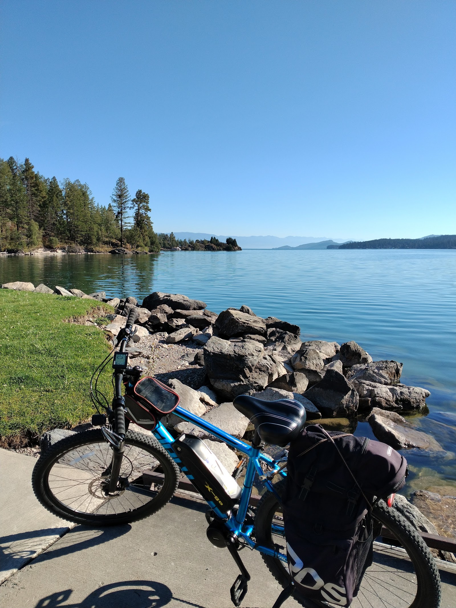 Blue mountain bike with panniers parked on a concrete path beside a rocky shore and calm lake in Glacier National Park.