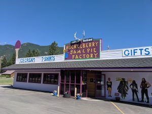 Colorful storefront with purple trim and a large hysterically bright sign for a huckleberry shop in Glacier National Park, with mountains in the background.