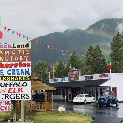 Colorful roadside gift shop with rainbow over green pines and distant Glacier peaks in Glacier National Park.