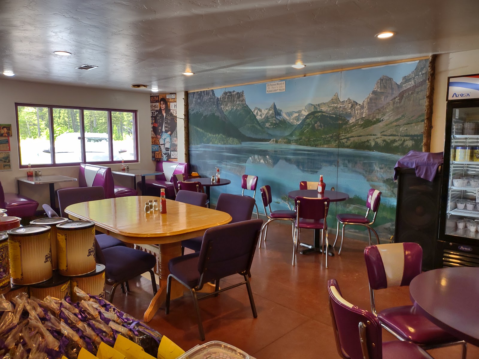 Interior view of a Glacier National Park gift shop with purple booths, round tables, and a large mural of mountains and a lake.