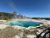 Yellowstone National Park geothermal pool in the Grant Visitor Center area with a vivid blue center and mineral terraces under a clear sky.