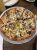Cheesy pizza loaded with yellow peppers, onions, olives and meat slices on a round metal tray in Yellowstone National Park.