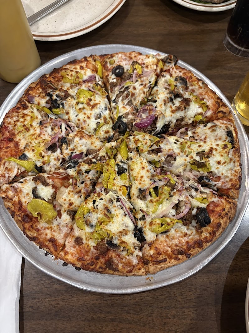 Cheesy pizza loaded with yellow peppers, onions, olives and meat slices on a round metal tray in Yellowstone National Park.