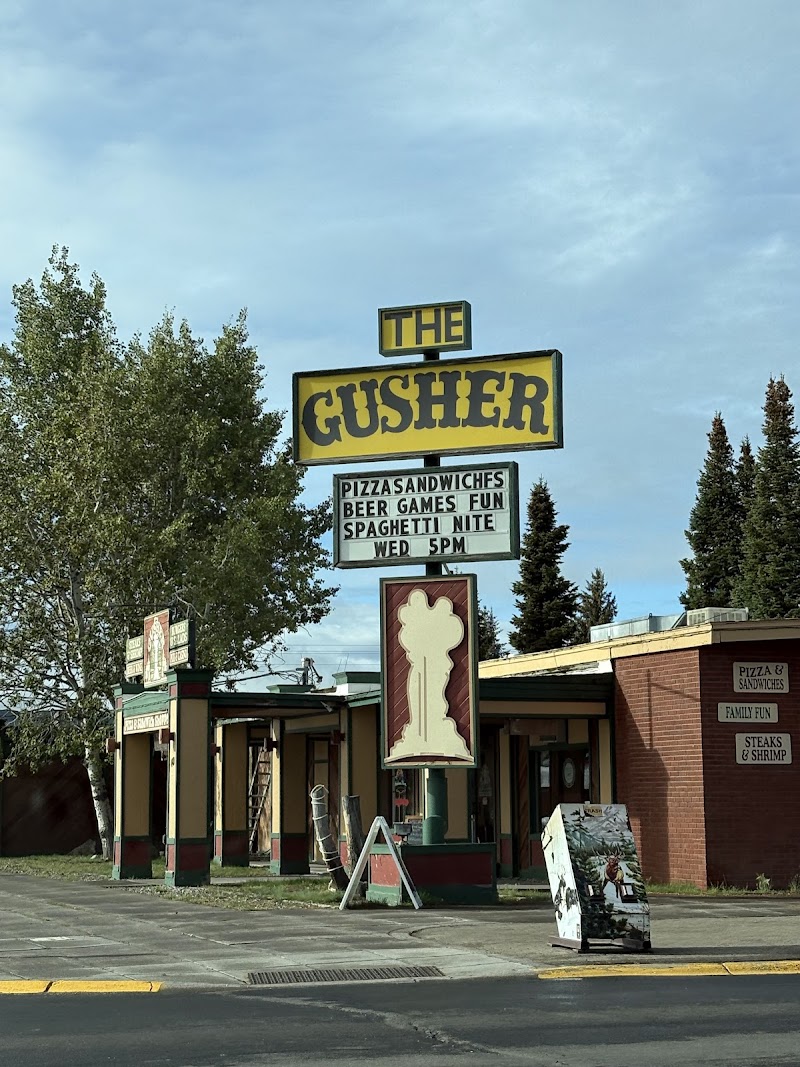 Yellowstone National Park roadside eatery with a tall retro sign, large yellow-green letters, brick building, and surrounding trees under a blue sky.
