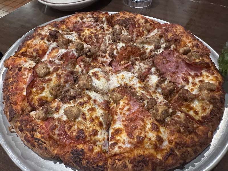 Large pepperoni and sausage pizza with melted cheese on a metal tray in a casual Yellowstone National Park restaurant.