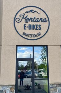 E-Bikes gift shop exterior in Glacier National Park, with round logo on a beige stucco façade.