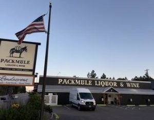 Frontage of a liquor and wine shop along the main road in Glacier National Park, with an American flag overhead.