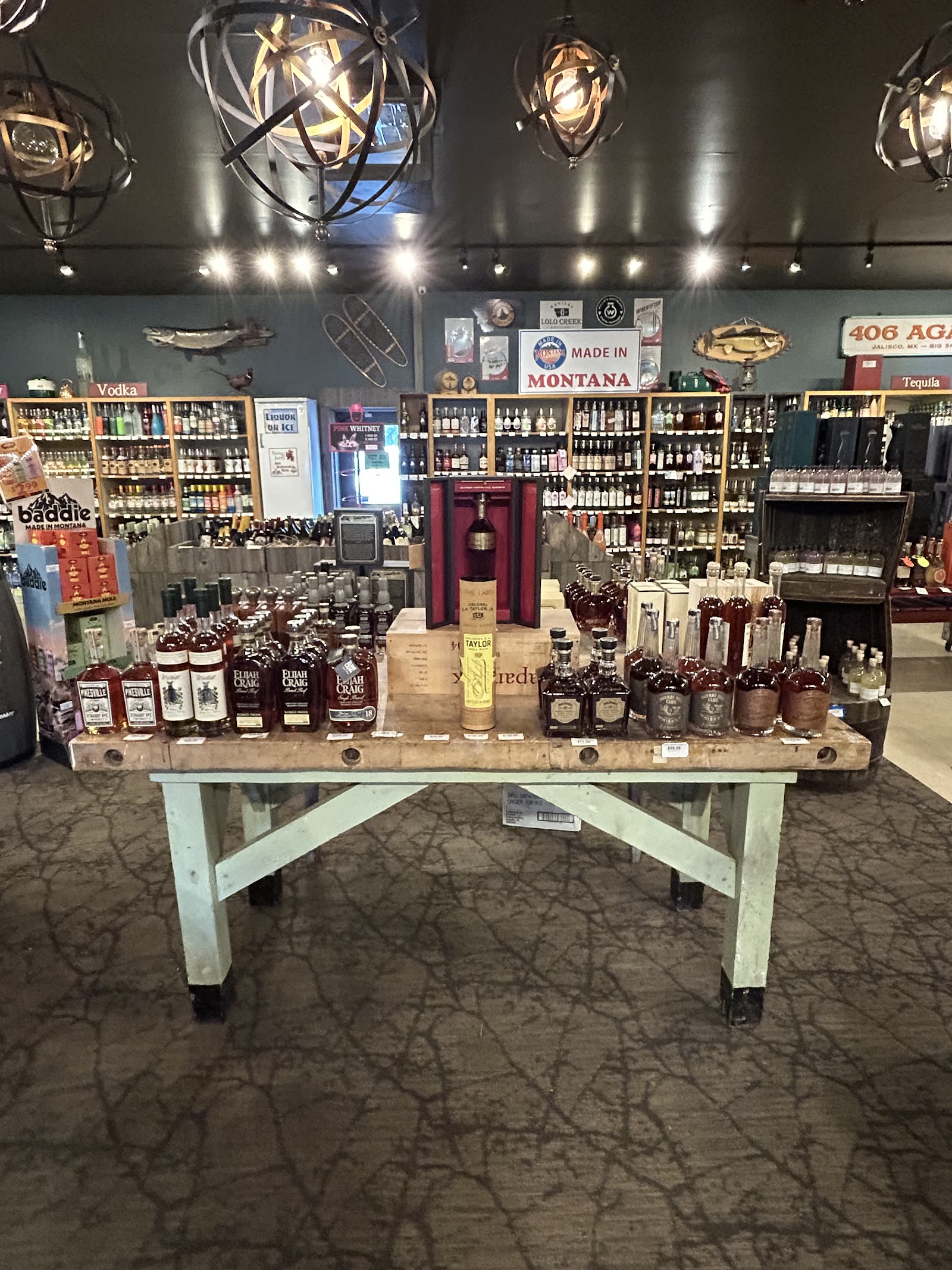 Interior view of a Glacier National Park liquor store with a long wooden table showcasing assorted bottles.