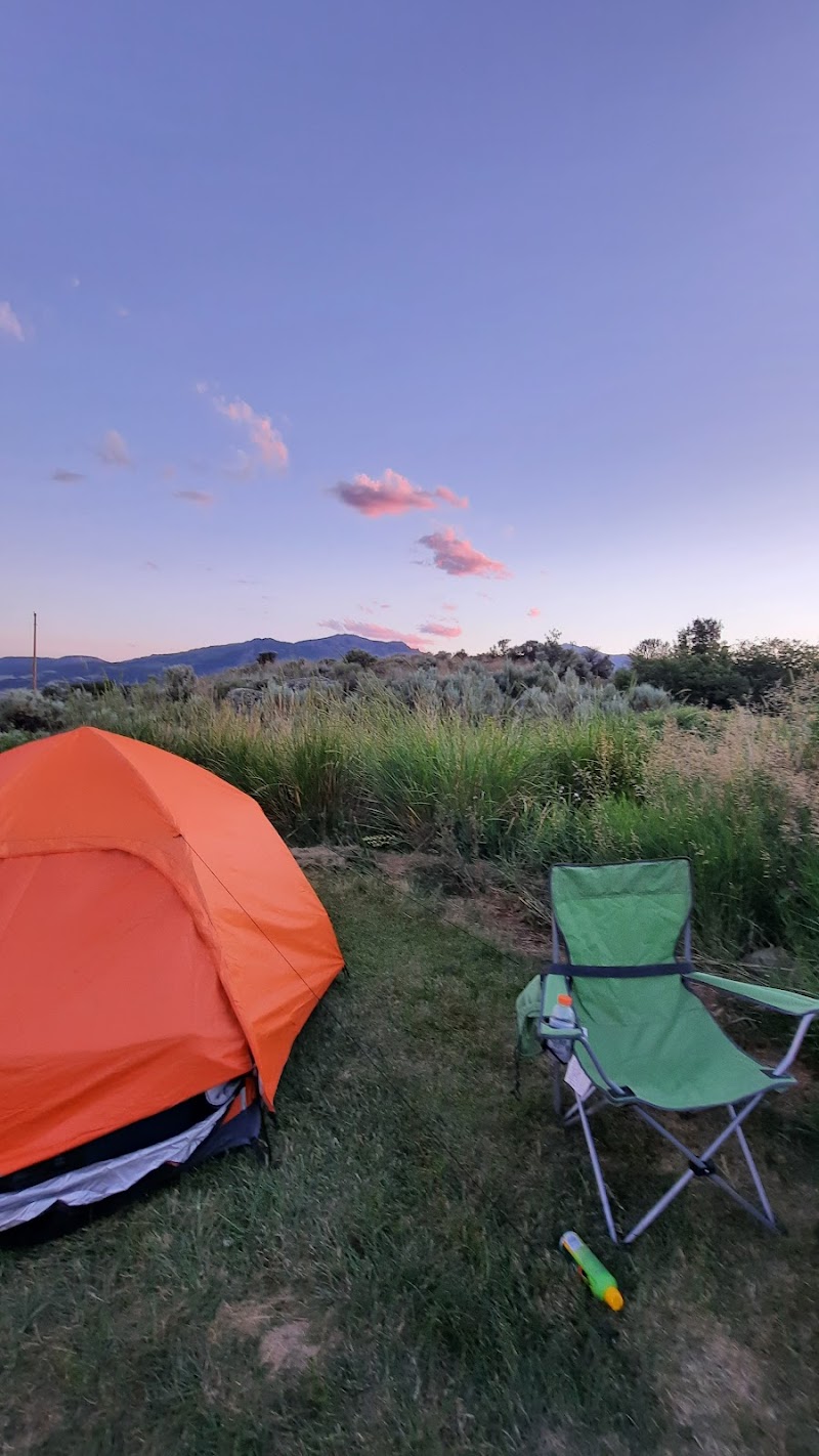 Orange tent and green camp chair on grassy campsite at sunset with distant mountains in Yellowstone National Park.