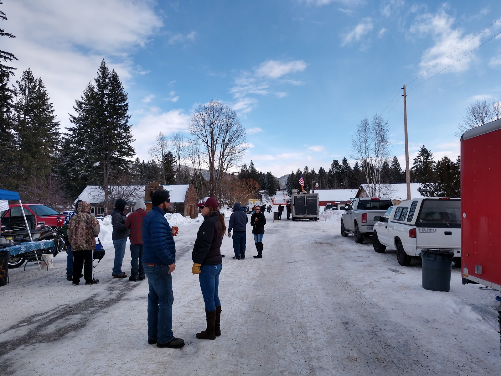 Snowy street scene outside South Fork Saloon in Glacier National Park, Montana, with visitors and parked vehicles along a snow-covered road.