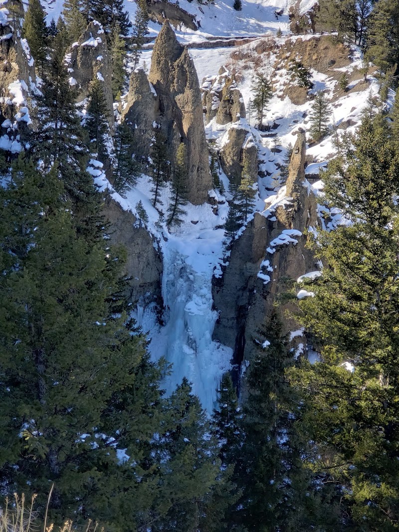 Tower Fall drops through jagged rock spires, with snow, evergreens, and blue ice in Yellowstone National Park.