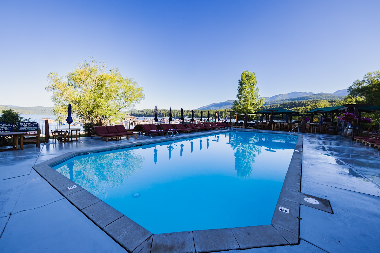 Outdoor pool area at a lodge with lounge chairs, umbrellas, and a lakeside view in Glacier National Park.