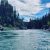 Turquoise Flathead River along forested banks in Glacier National Park, with rocky shores and blue sky.