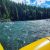 Yellow raft glides along the turquoise Flathead River beside a dense evergreen shoreline in Glacier National Park.