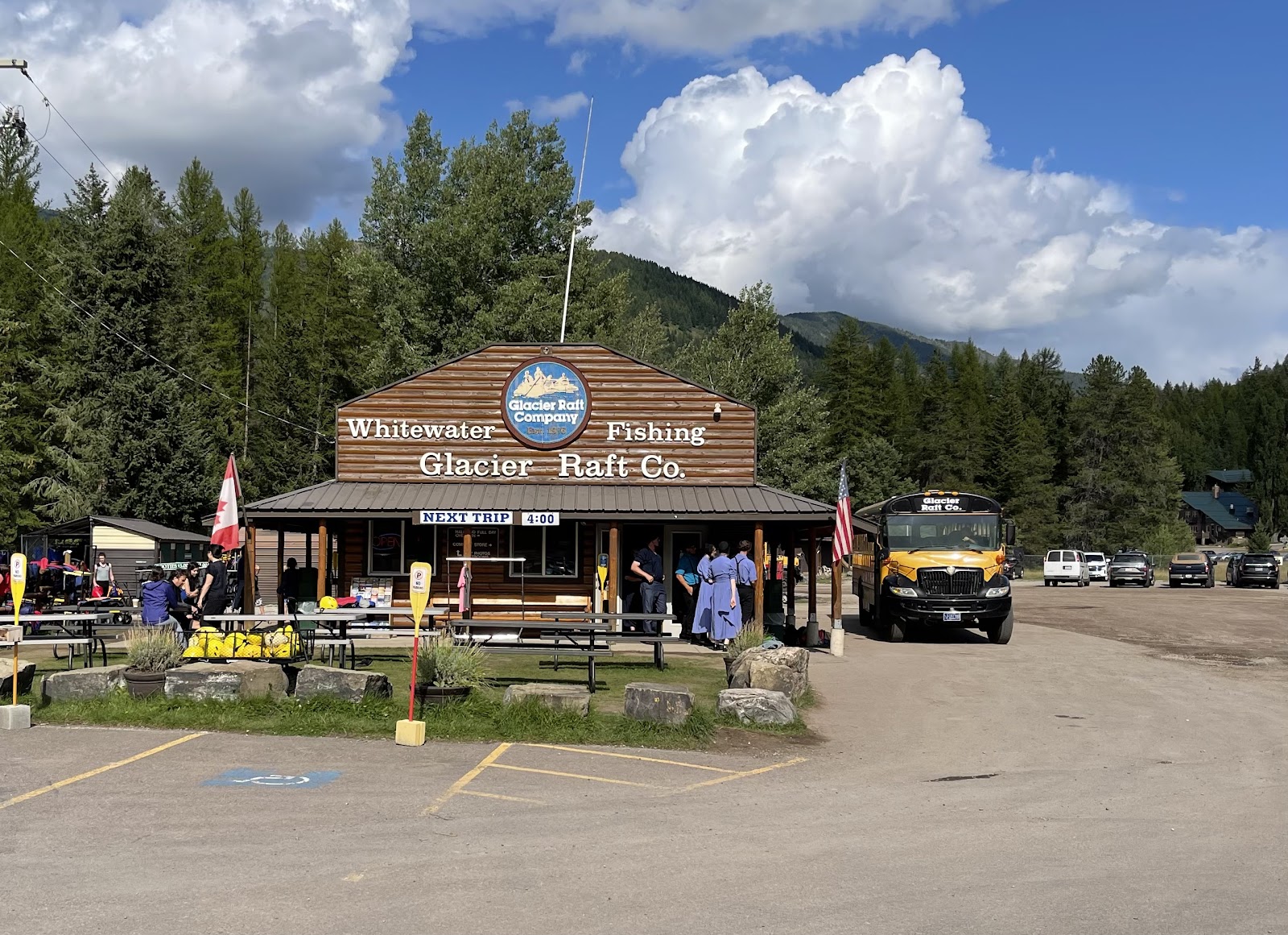 Whitewater rafting facility at Glacier National Park with a wooden building, buses, and people outside on a sunny day.