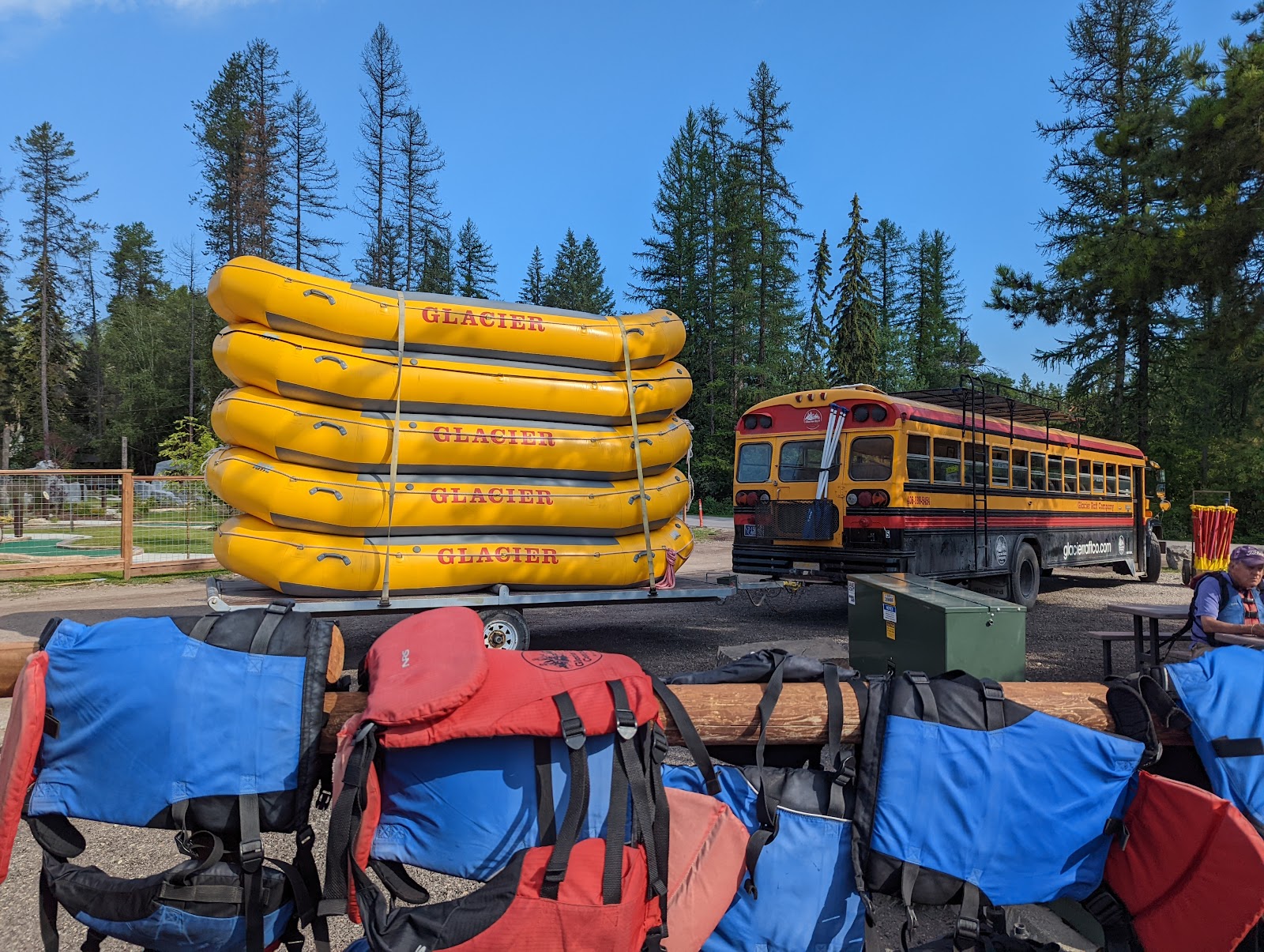 Glacier National Park rafting gear yard with stacked yellow inflatables and a vintage bus in the background.